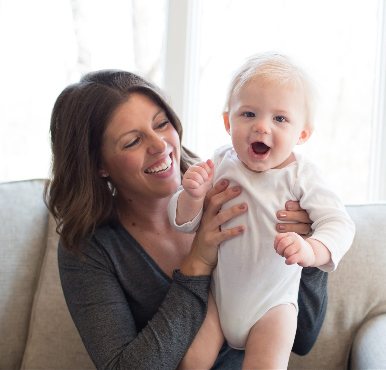 Smiling mom holding happy baby on couch